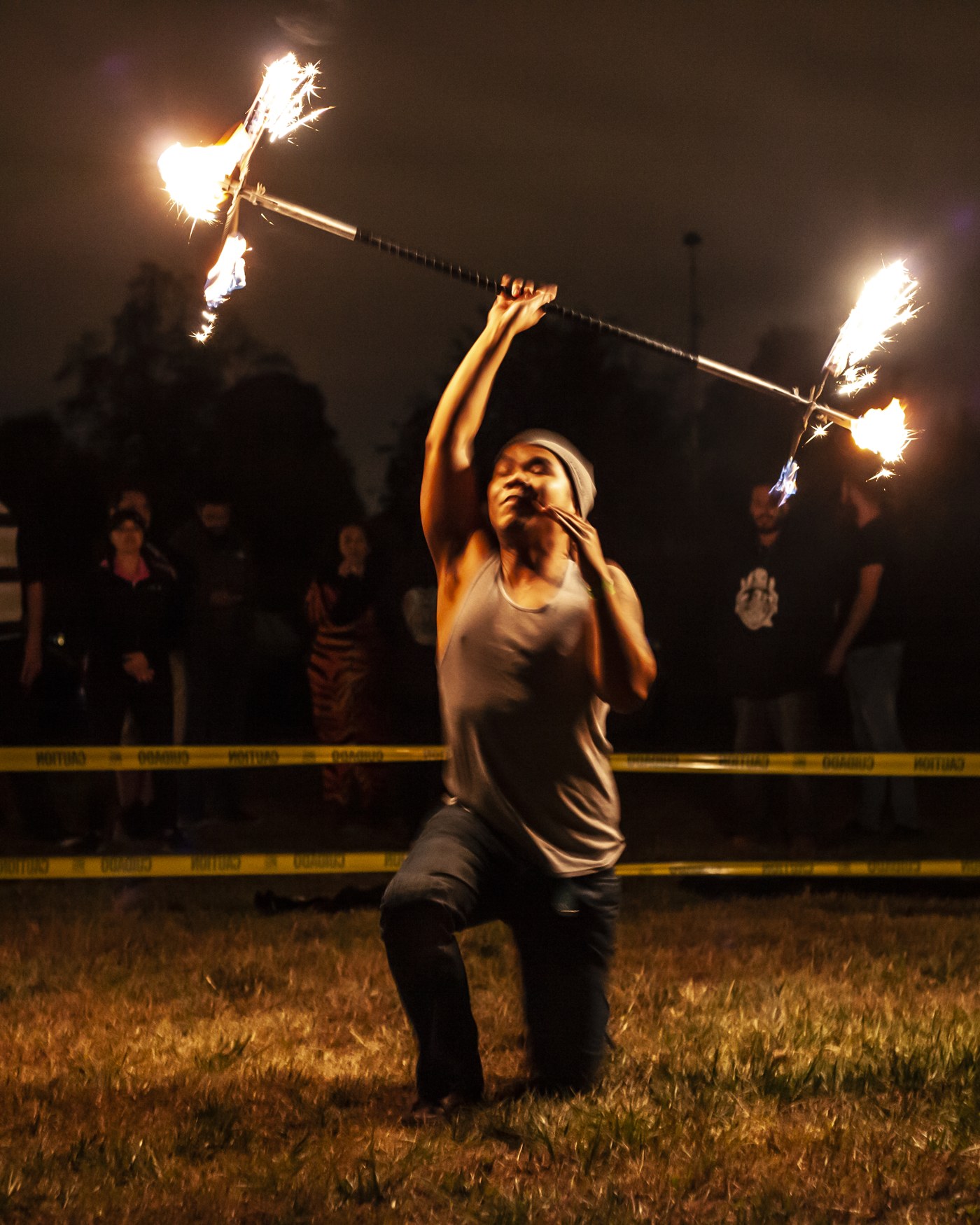 Fire performer mid-spin at a live Optical Illusions event, crowd watching behind safety lines.